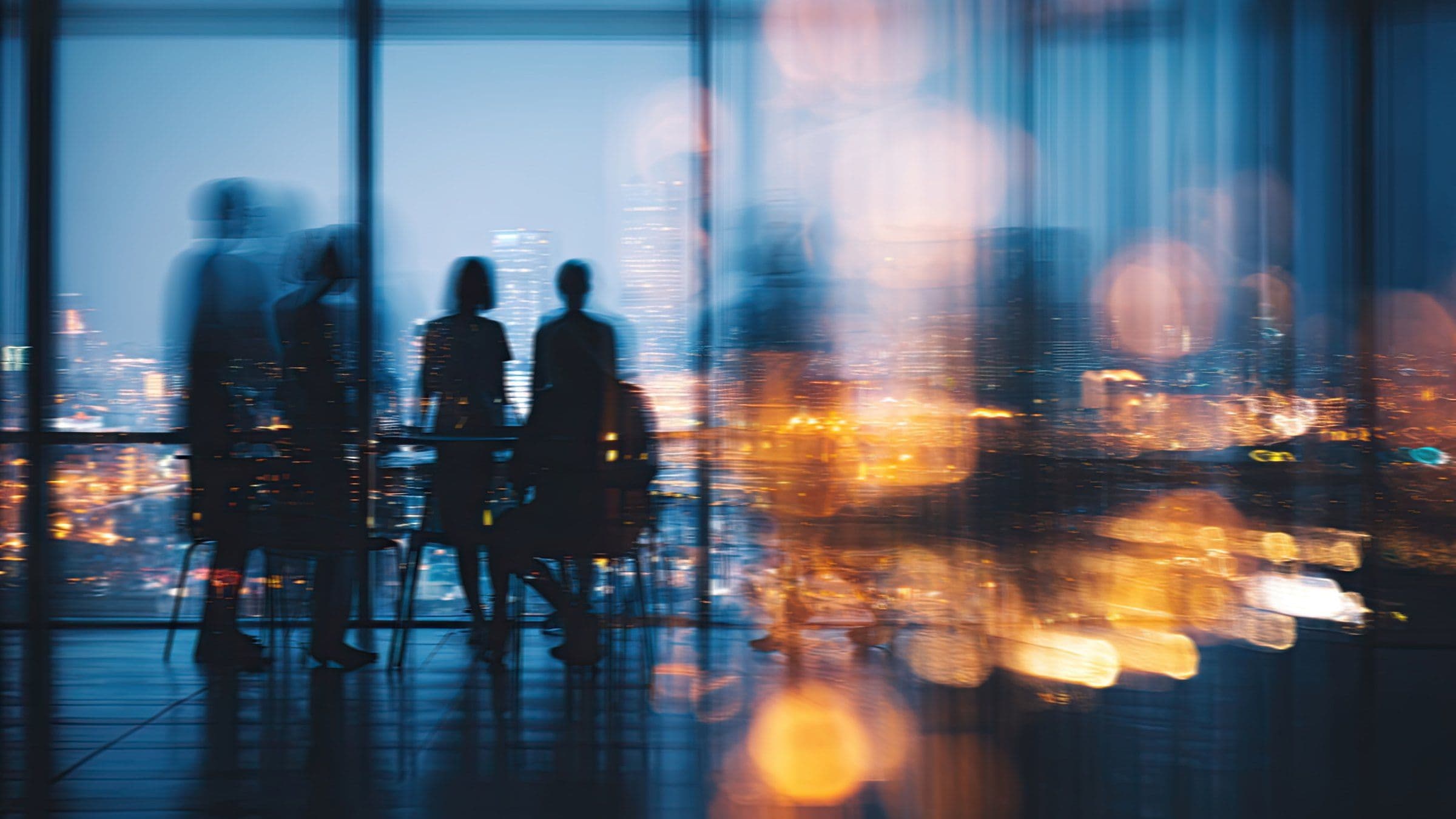 Silhouettes of a leadership team meeting in a glass-walled office overlooking city lights at dusk