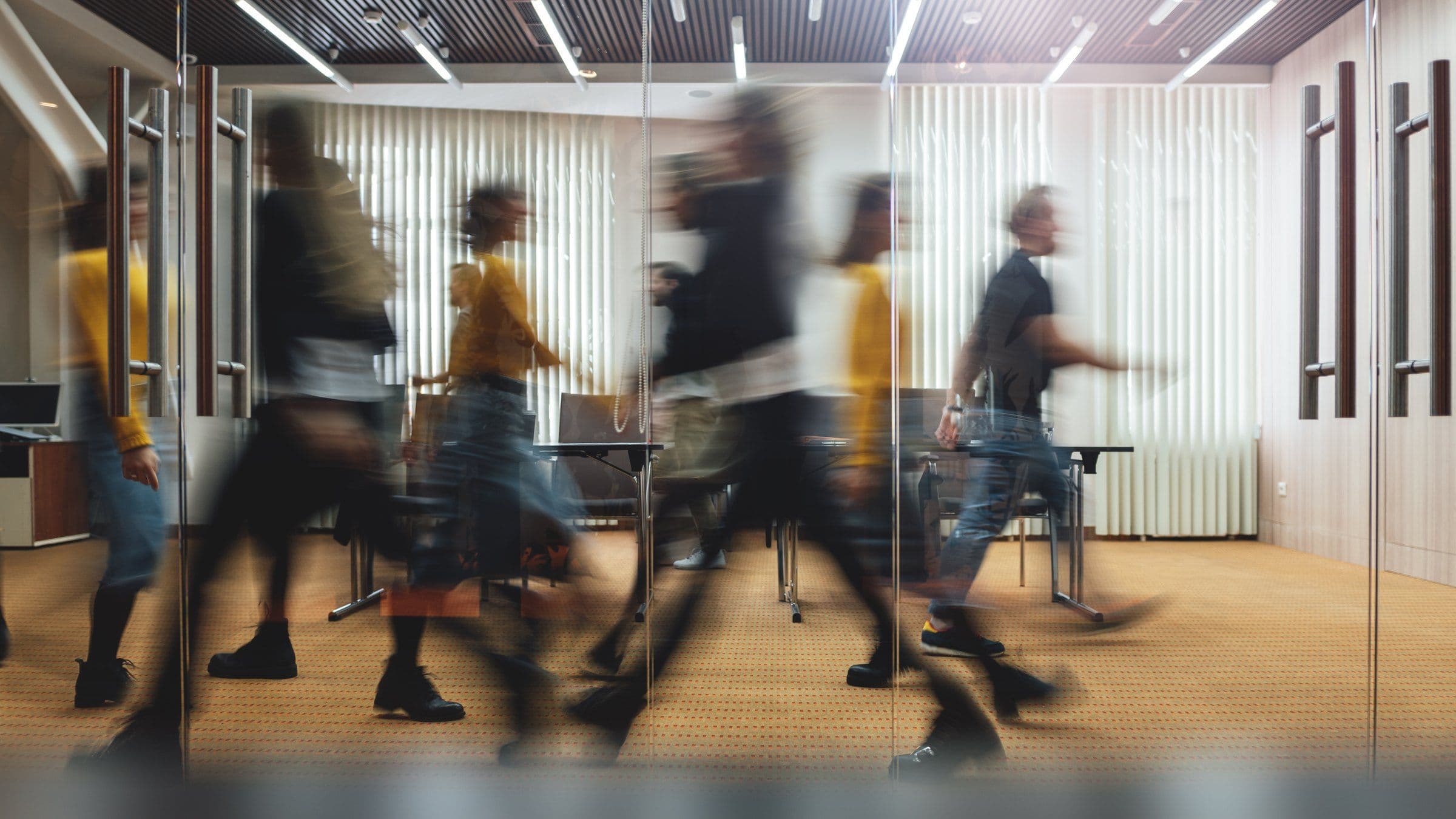 Motion-blurred team walking past glass doors through a bright modern office