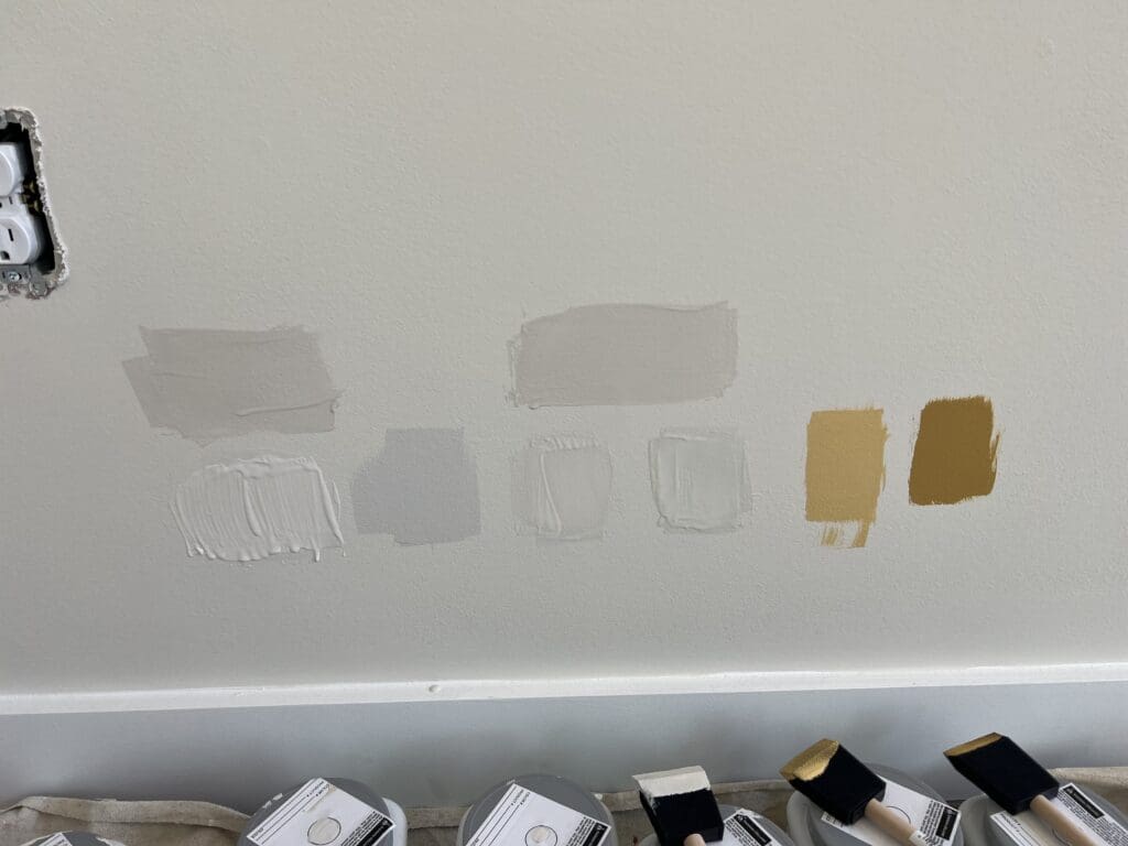 Wall displaying multiple paint color swatches in various shades: gray, neutral tones, and golds arranged in a grid pattern.